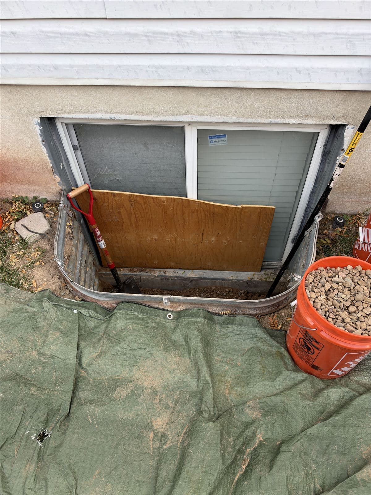 Job site prepped with a tarp over the lawn, hand tools, and a bucket of drainage gravel